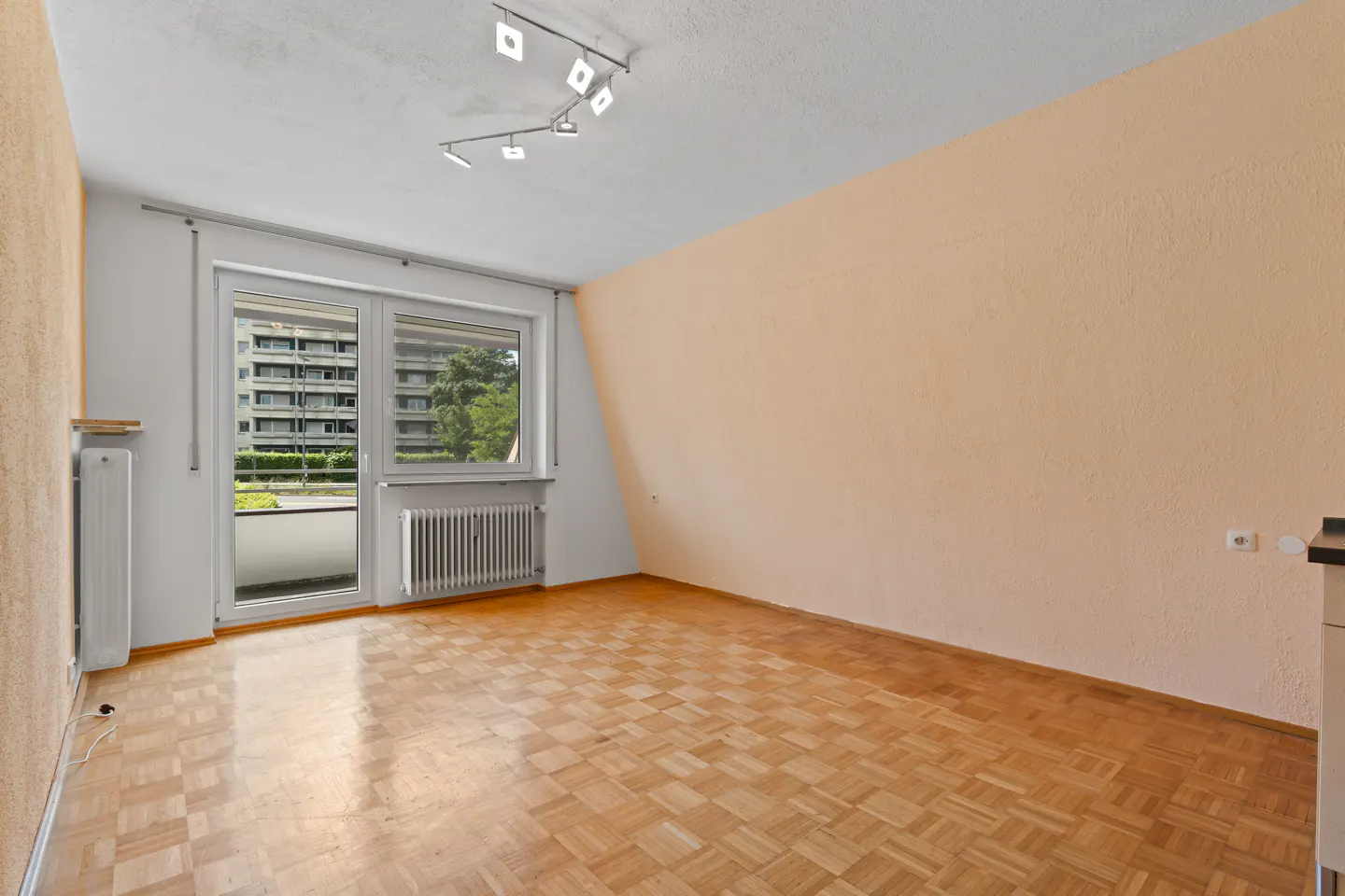 Empty room with light peach walls, parquet flooring, a balcony door, and a modern ceiling track light.