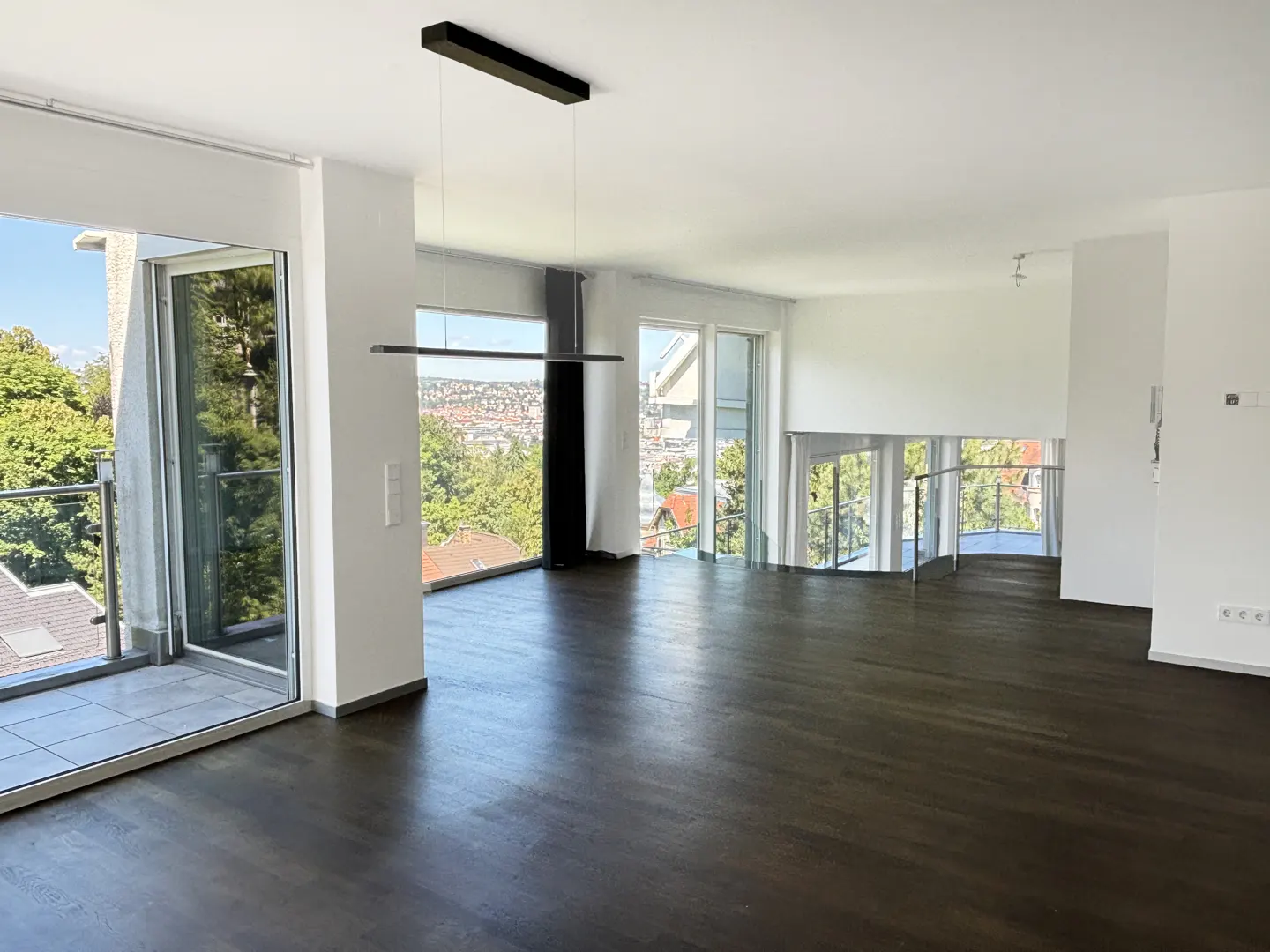 Bright, modern living room with dark wood floors, white walls, and large windows with a city view. A black linear light fixture hangs from the ceiling.