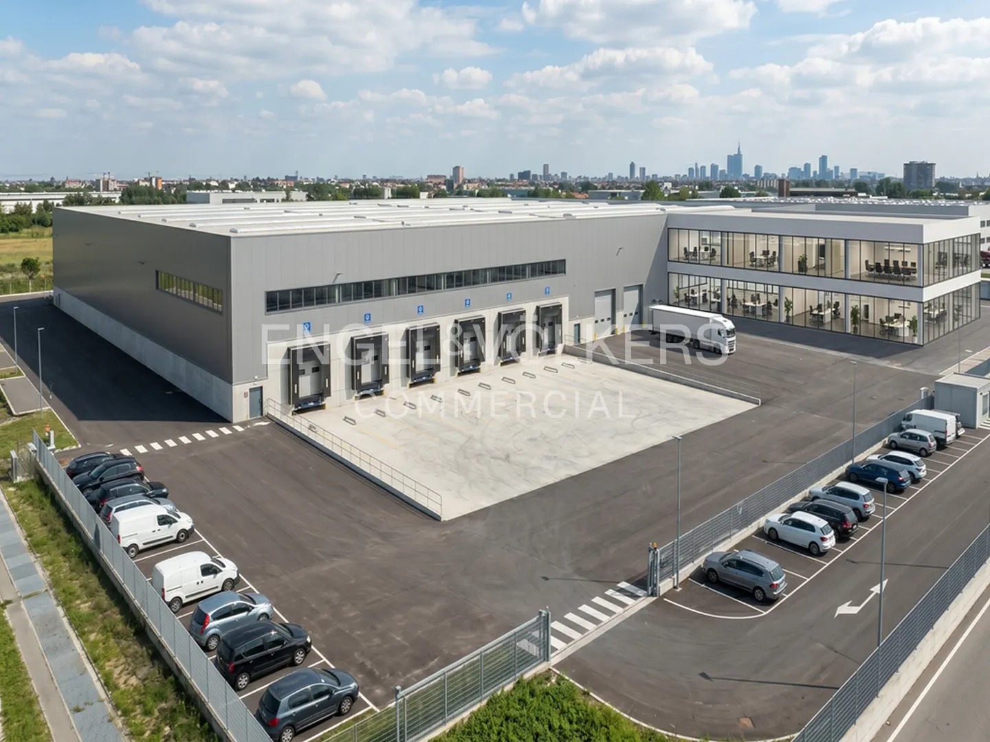 Aerial view of a gray warehouse with loading docks, parking, and office space. City skyline in the background.