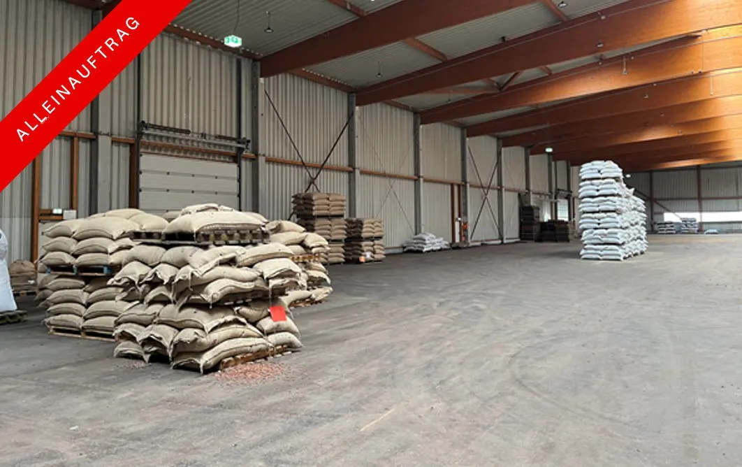 A warehouse interior with stacks of burlap sacks on pallets, under a high ceiling with wooden beams.