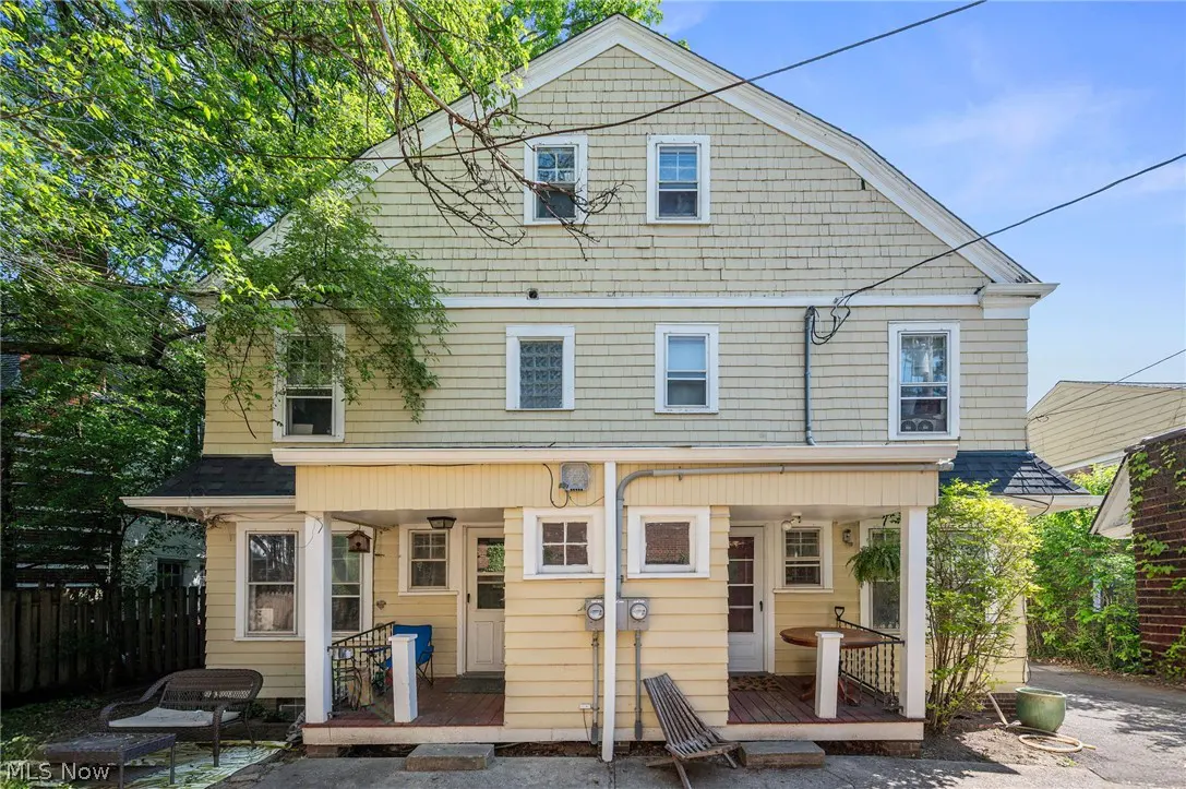 Exterior of a two-story, yellow duplex with porches, windows, and green trees.
