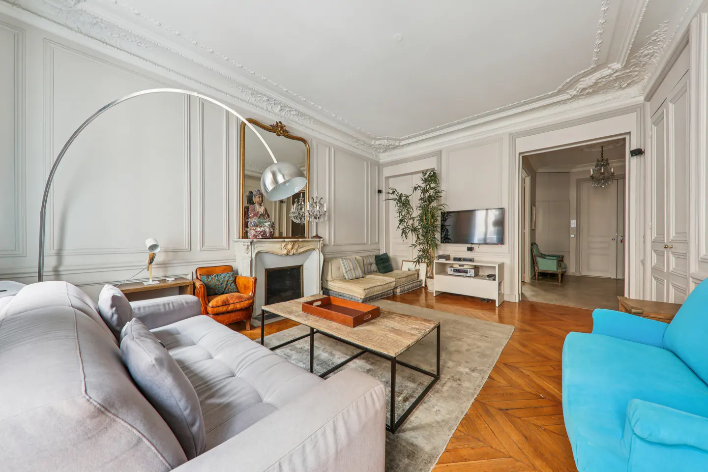 Elegant living room with a grey sofa, bright blue armchair, fireplace, ornate mirror, and hardwood floors.