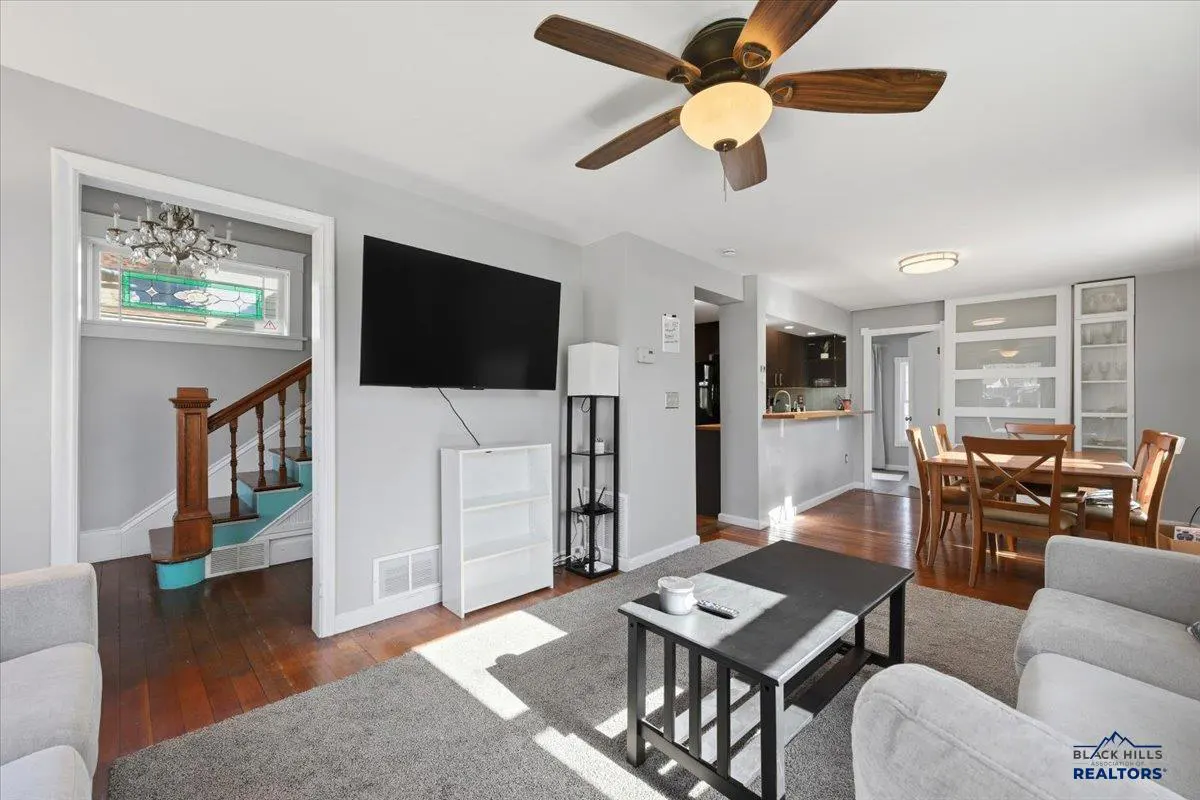 A living room with gray walls, a ceiling fan, a TV, a staircase, and a dining area.