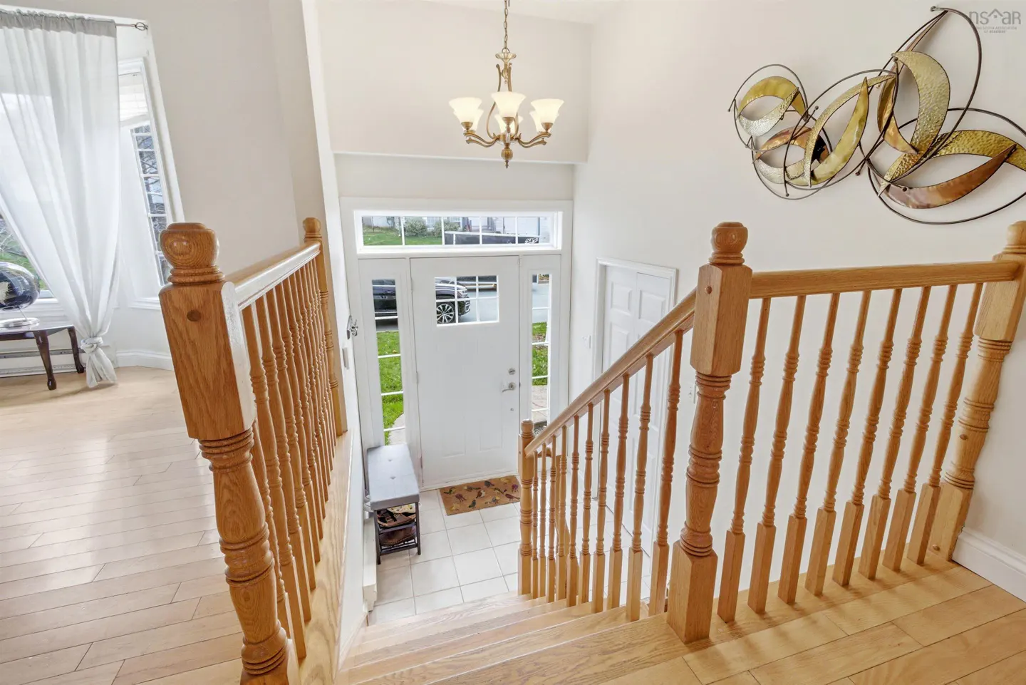View from the top of wooden stairs, looking down to a white front door with glass panels. A chandelier hangs above.