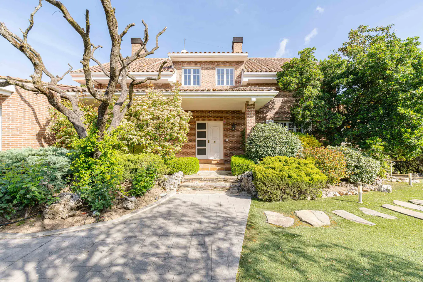 Brick house with a white door, tile roof, and green landscaping. A stone path leads to the entrance.