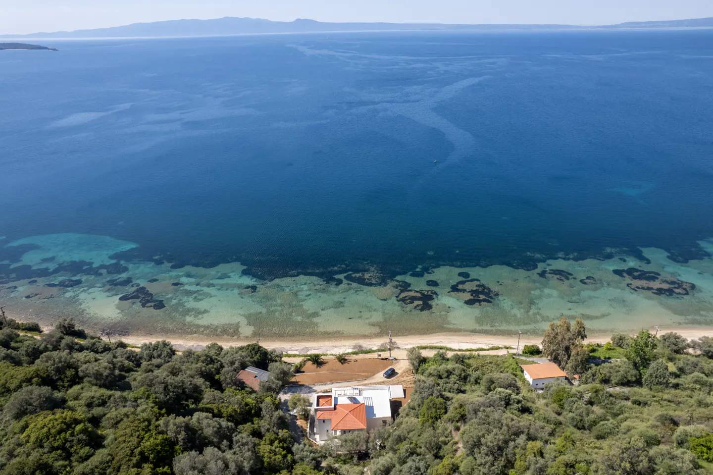 Aerial view of a modern house with a red tile roof near a sandy beach and blue ocean.