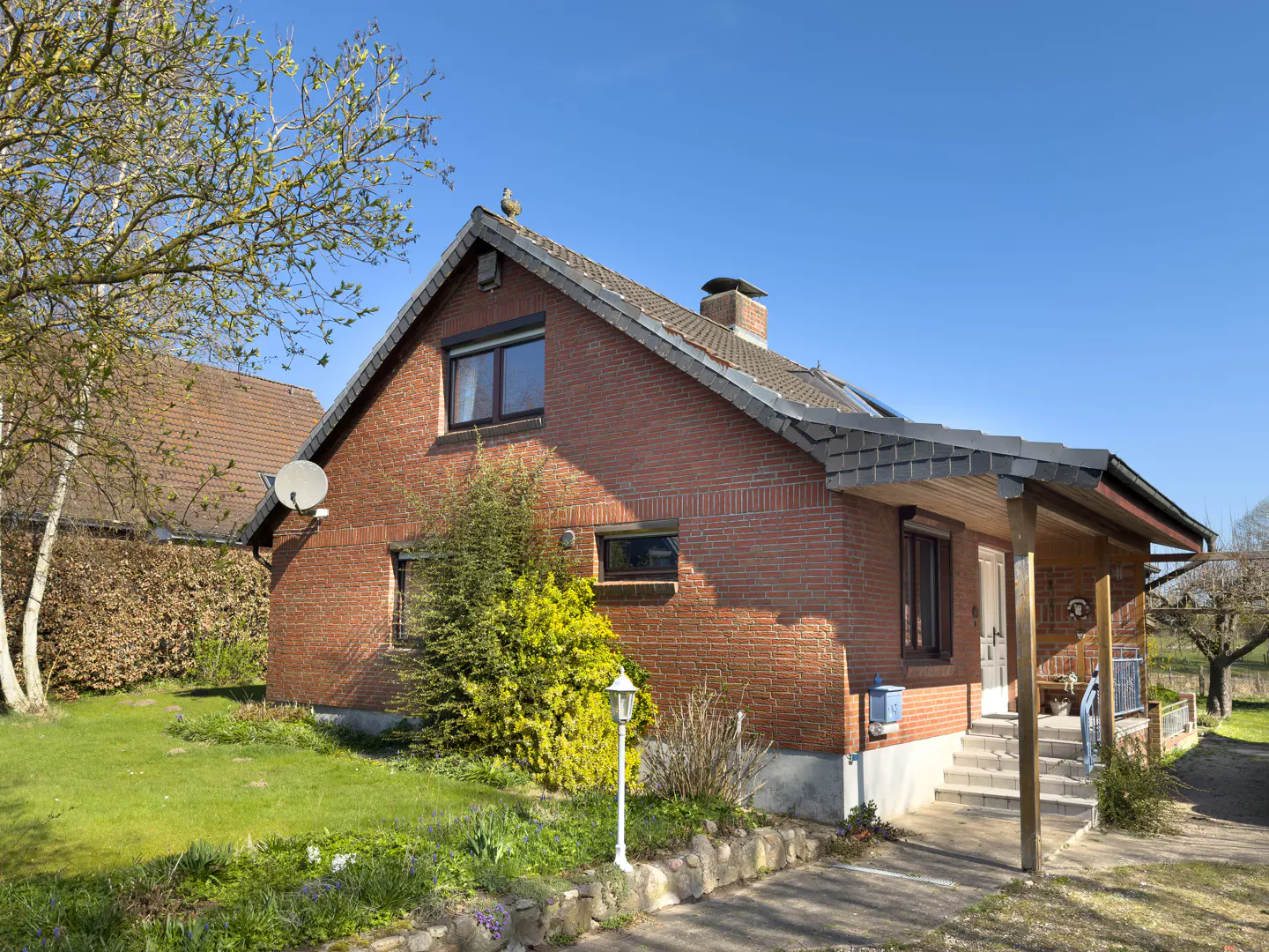 A red brick house with a gray roof and a small porch on a sunny day.