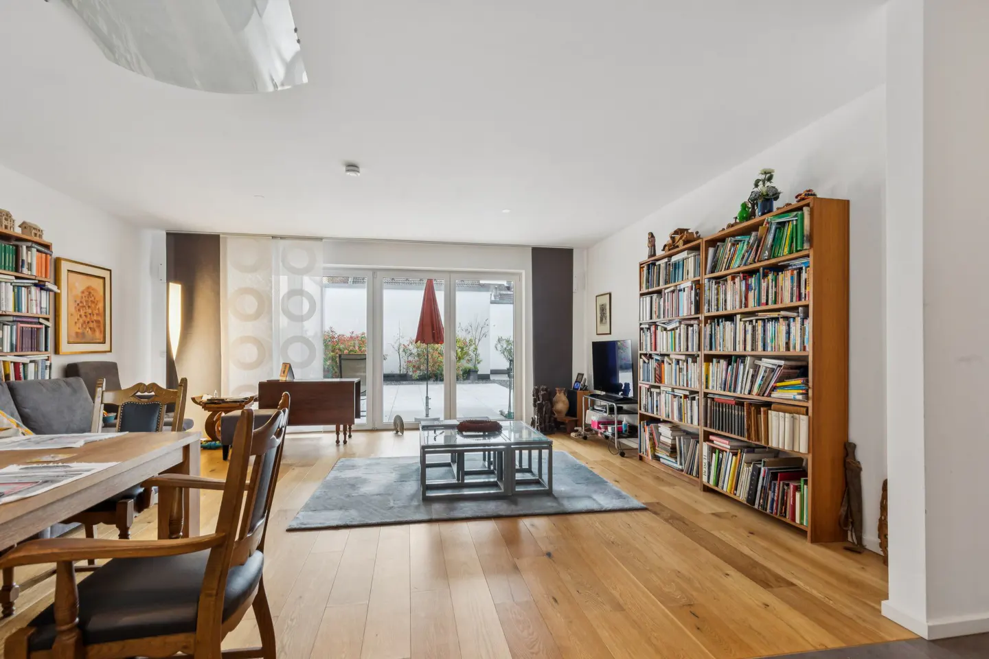 Bright living room with wood floors, a large bookcase, and a patio view through sliding glass doors.