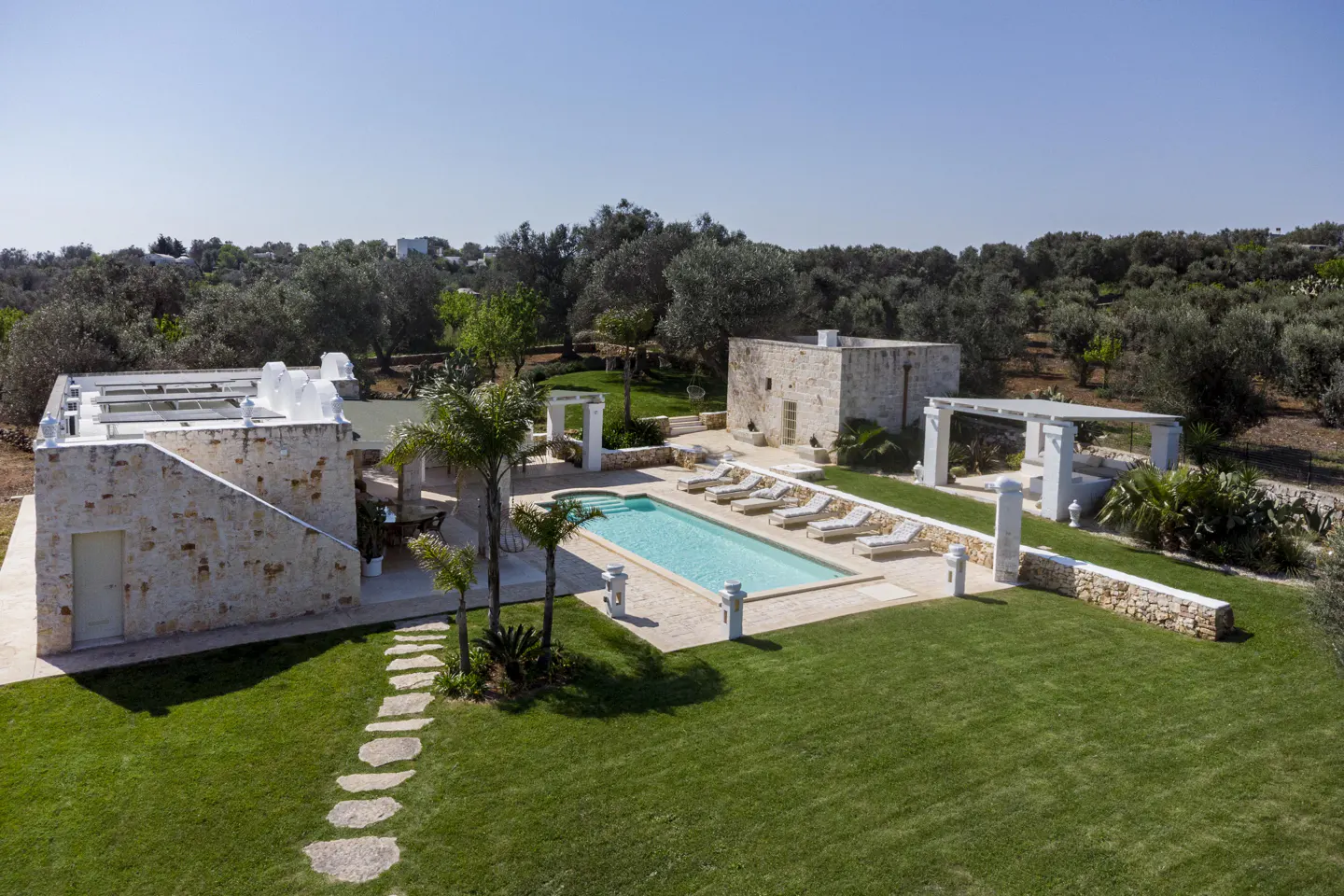 Aerial view of a stone house with a pool, lounge chairs, and green lawn on a sunny day.