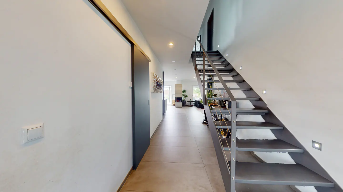 Modern hallway with light tile floors, a dark sliding door, and an open-tread metal staircase leading to an upper floor.