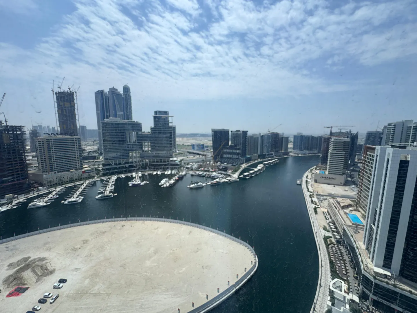 Cityscape view of Dubai with a marina, modern buildings, and a blue sky with scattered clouds.