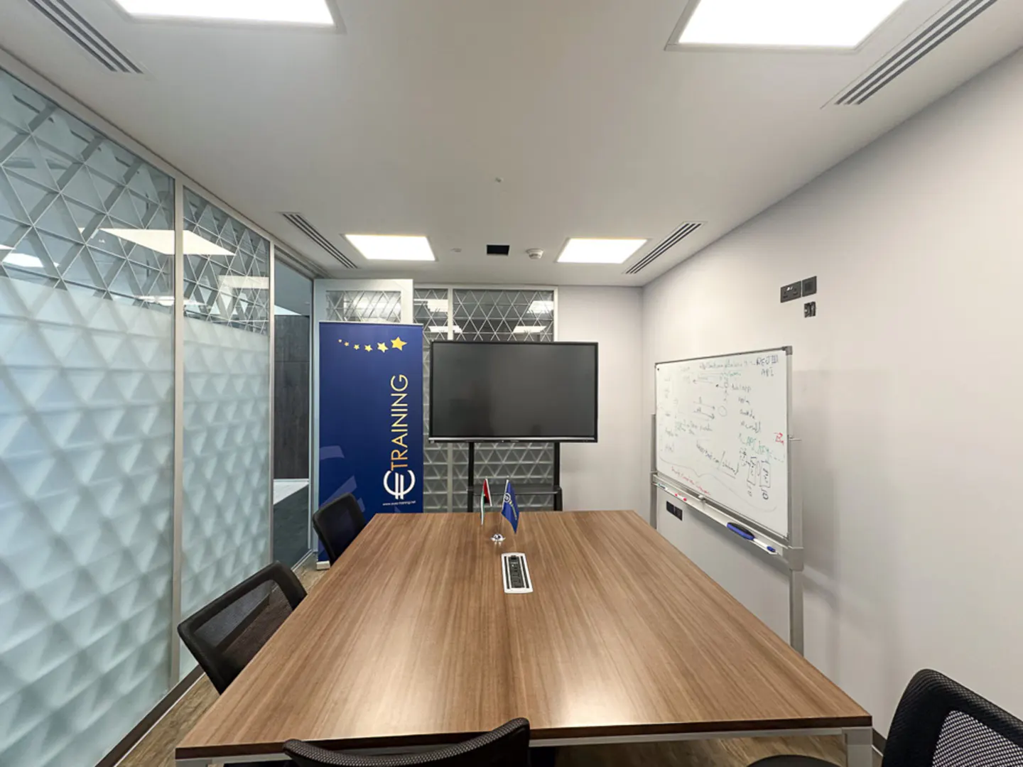 Conference room with a wood table, black chairs, a TV, and a whiteboard. A blue banner with "Training" is visible.
