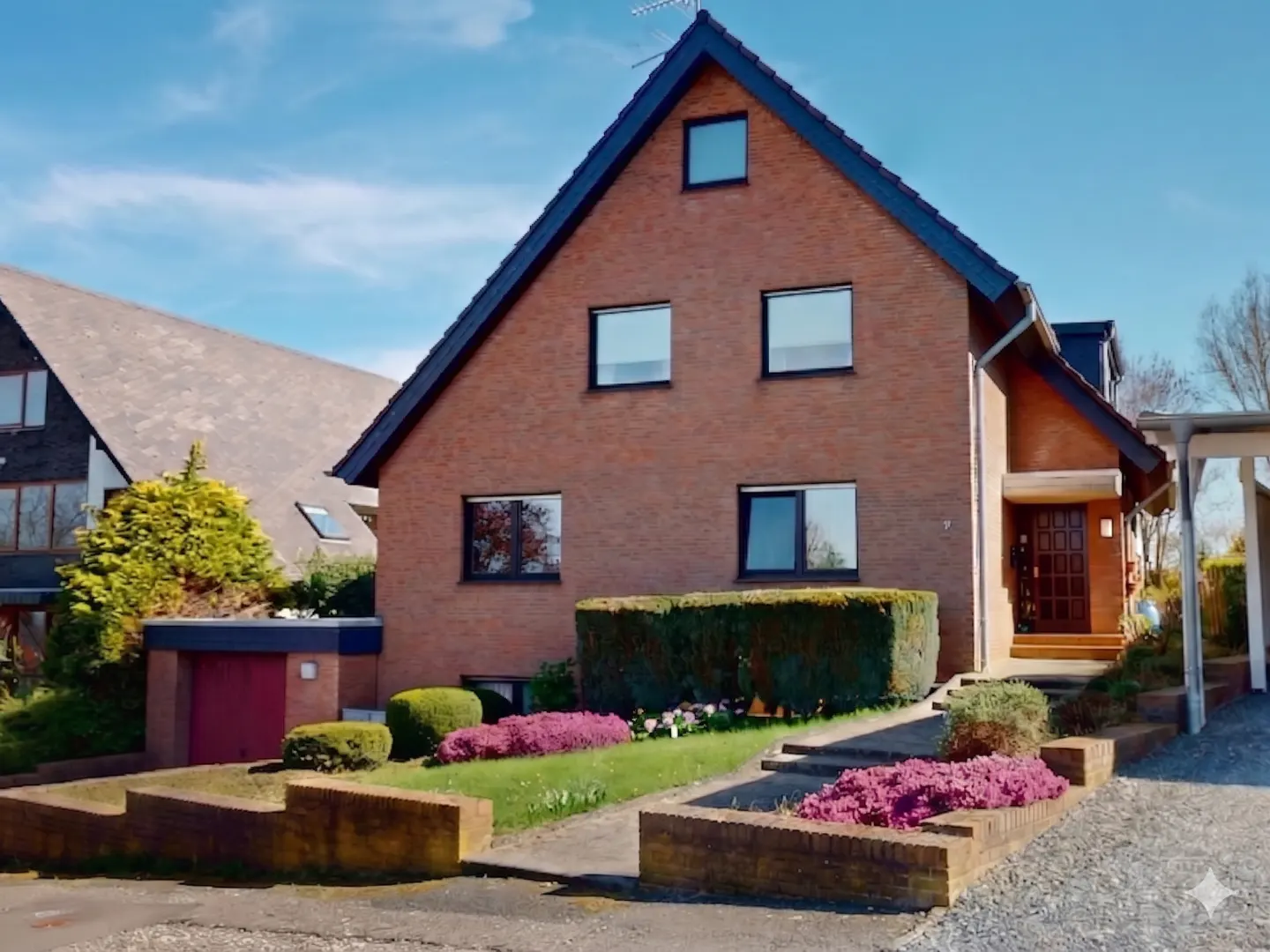 A two-story brick house with a dark roof and a well-manicured lawn on a sunny day.
