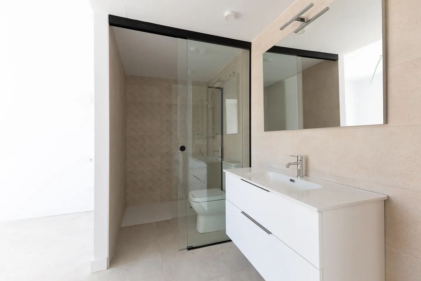 Modern bathroom with a white vanity, wall mirror, and a glass-enclosed walk-in shower with beige tiled walls.
