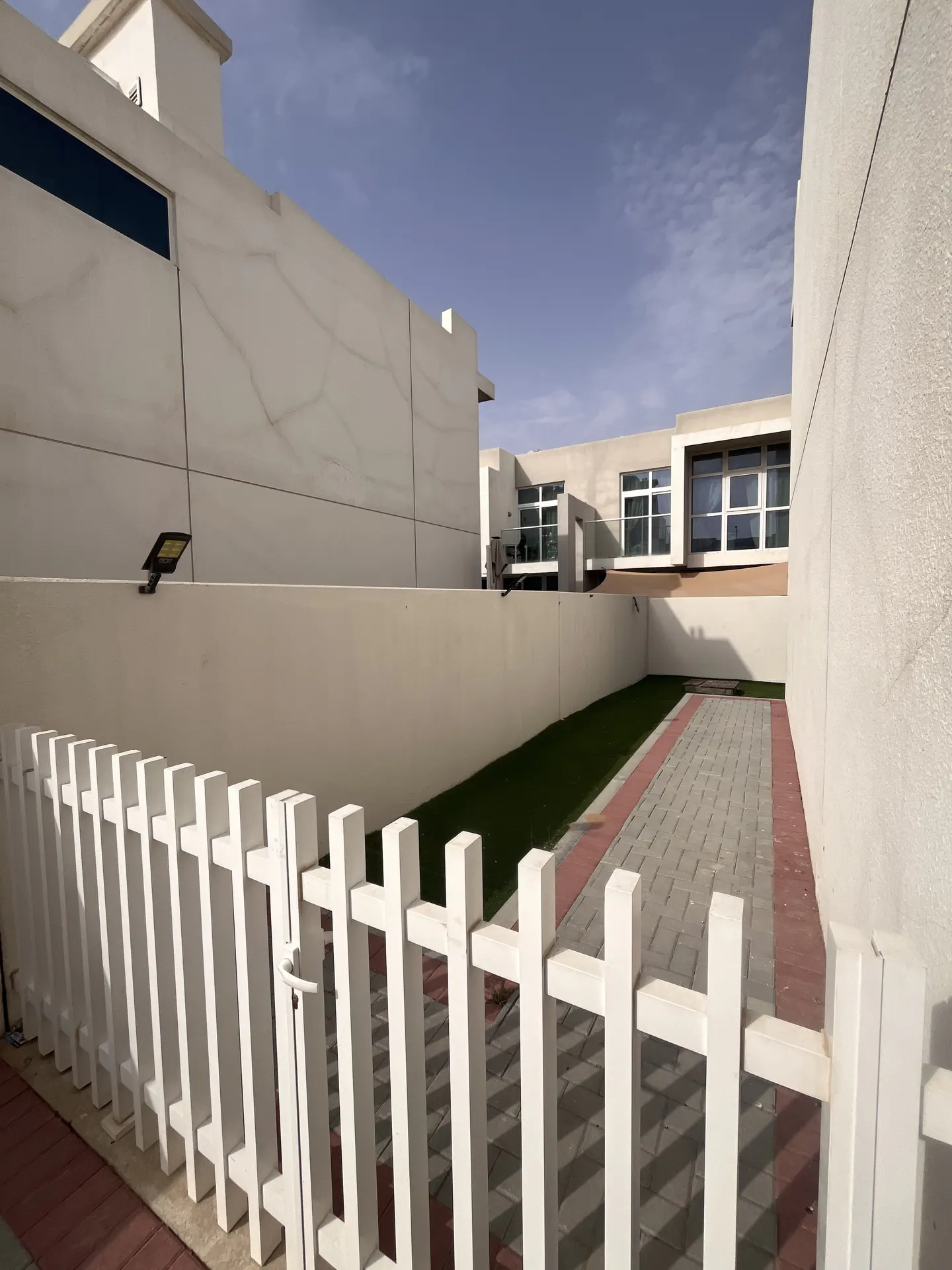 Exterior view of a modern white house with a white picket fence, a brick driveway, and a strip of green grass.