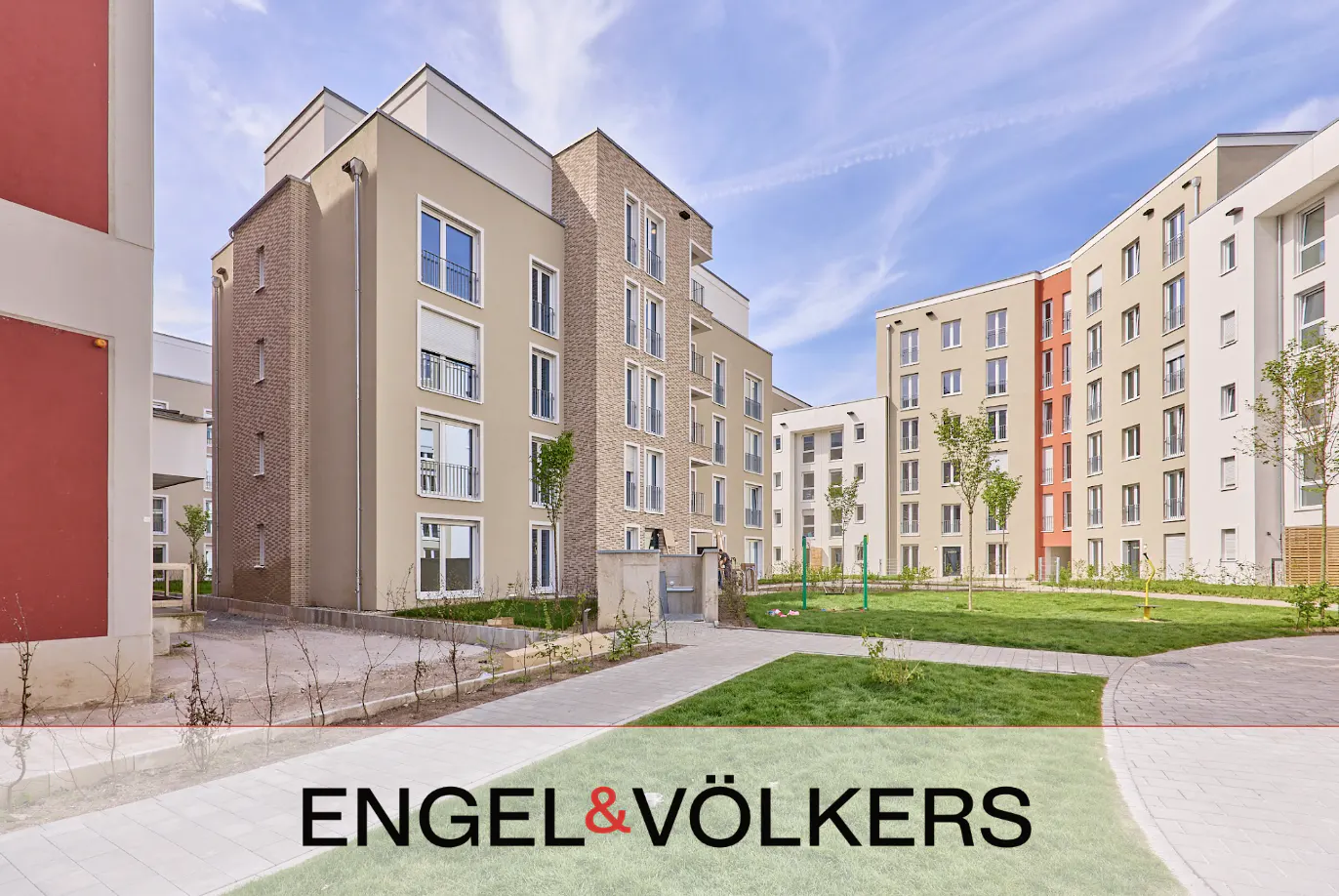 Modern apartment buildings with beige and red facades surround a central green courtyard under a clear blue sky.