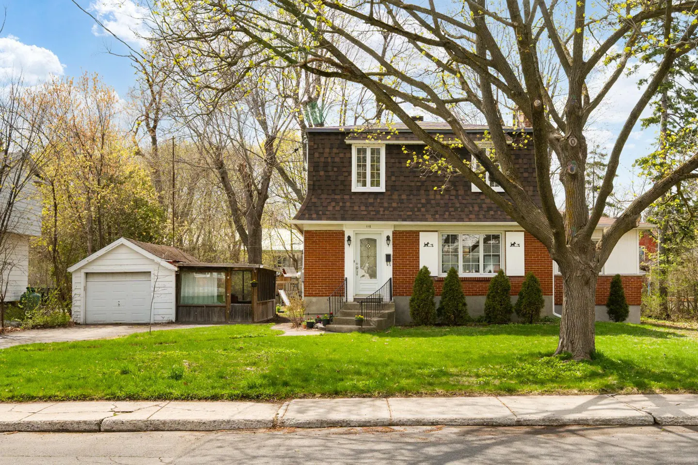 Two-story brick house with a brown roof, white trim, and a white garage on a green lawn.