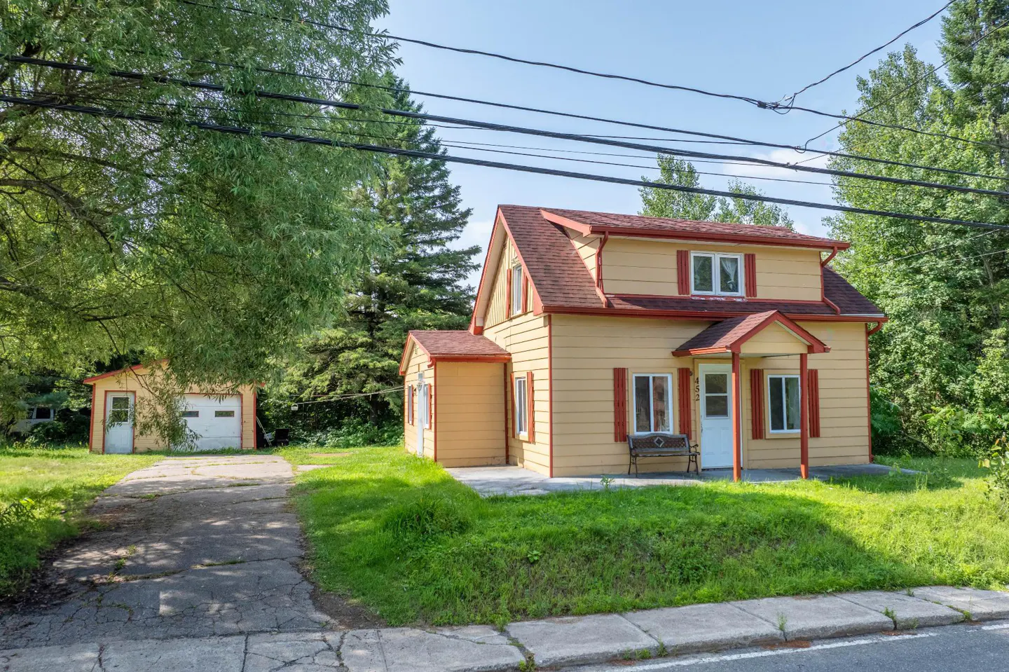 A yellow two-story house with red trim and a matching detached garage, set on a grassy lot with a concrete driveway.