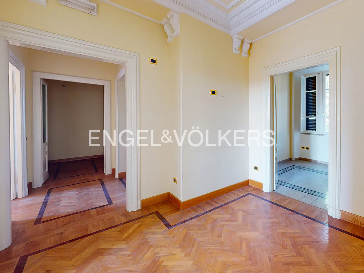 Empty room with pale yellow walls, ornate crown molding, and polished herringbone wood floors with dark wood borders.