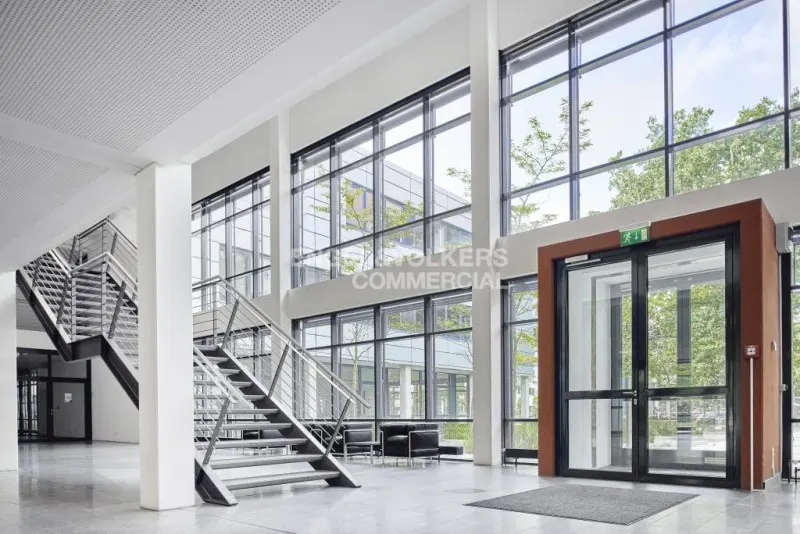 Bright, modern lobby with large windows, metal stairs, and a glass-door exit. The floor is polished concrete.