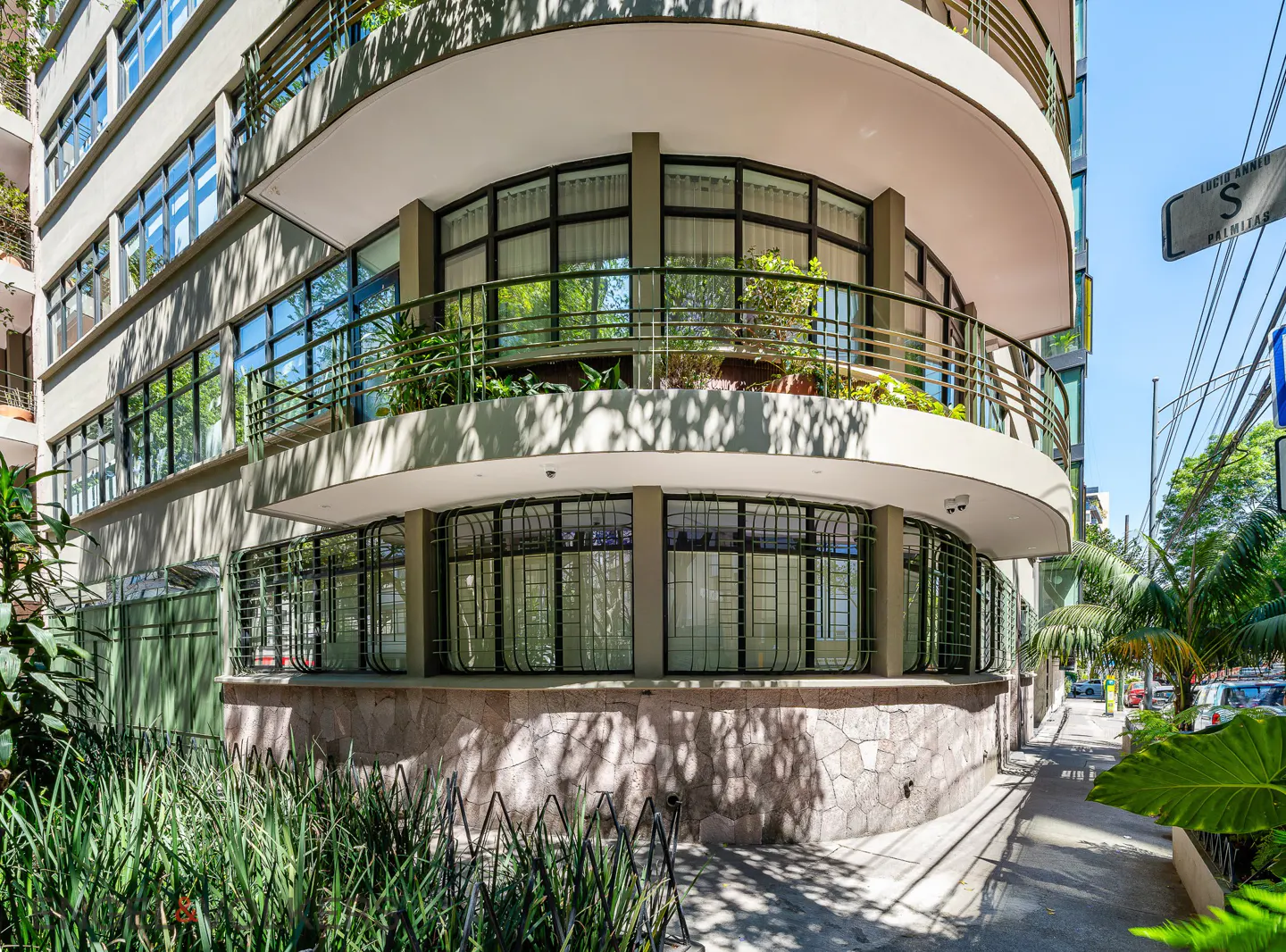 Exterior view of a curved, multi-story building with large windows and balconies, surrounded by lush greenery.