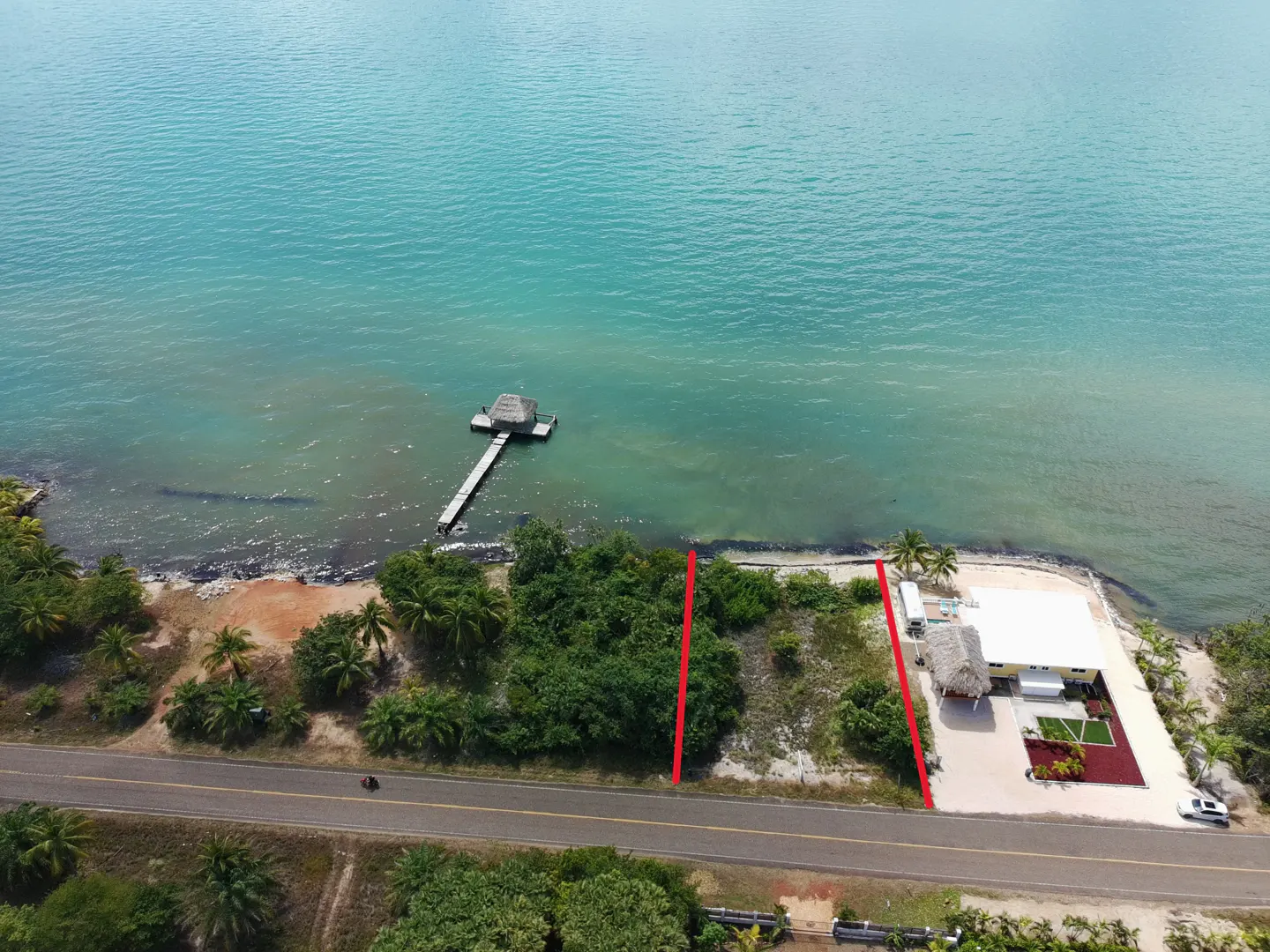 Aerial view of a waterfront property with turquoise water, a dock, and a building with a thatched roof. Red lines mark property boundaries.