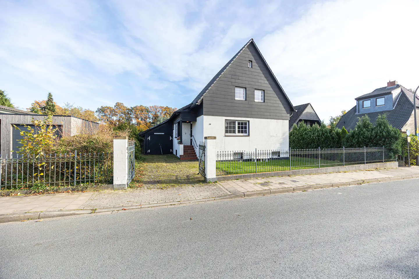 Two-story house with a black roof and white walls, surrounded by a black metal fence and green grass.