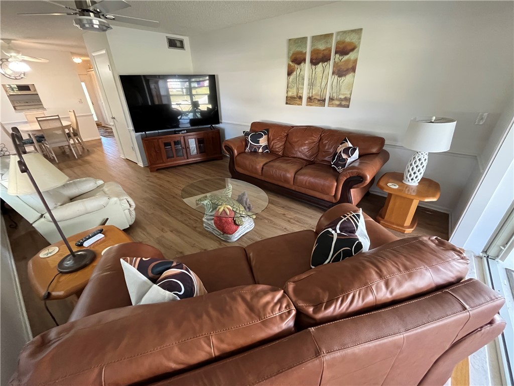 Living room with brown leather sofas, wood floors, and white walls. A TV sits on a wooden stand, and a glass coffee table is in the center.