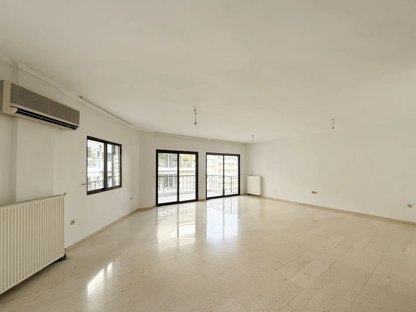 Bright, empty room with marble floors, white walls, and black-framed windows and sliding doors to a balcony.