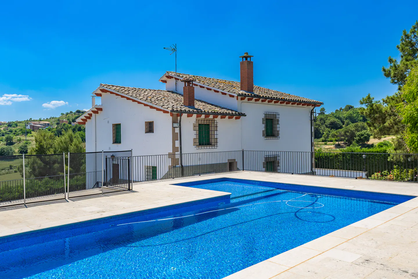 Exterior view of a white two-story house with a blue tiled pool in the foreground on a sunny day.
