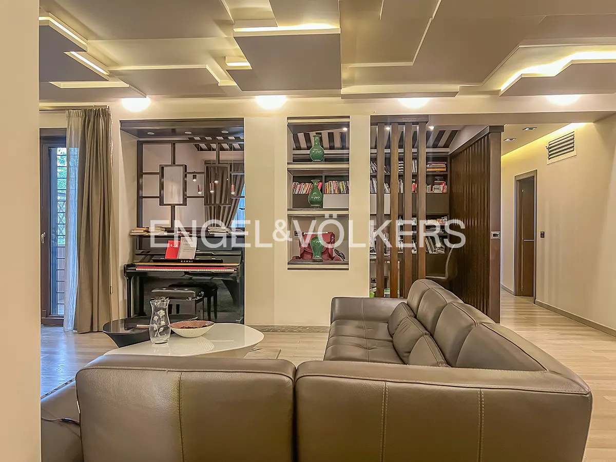 Living room with a brown leather sofa, piano, bookshelves, and decorative ceiling lights.