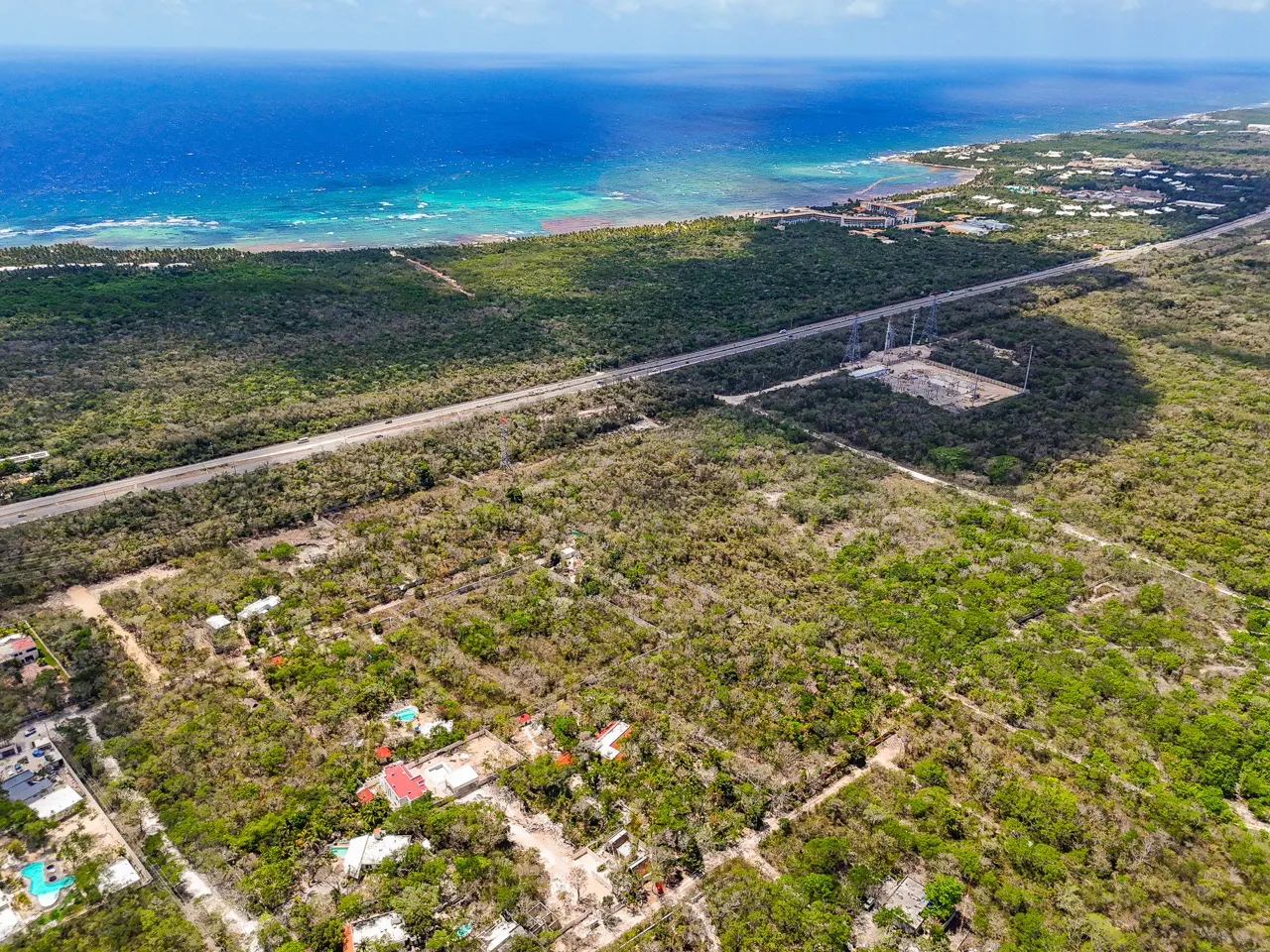 Aerial view of a tropical landscape with a highway, ocean, and scattered houses. Lush green vegetation covers the land.