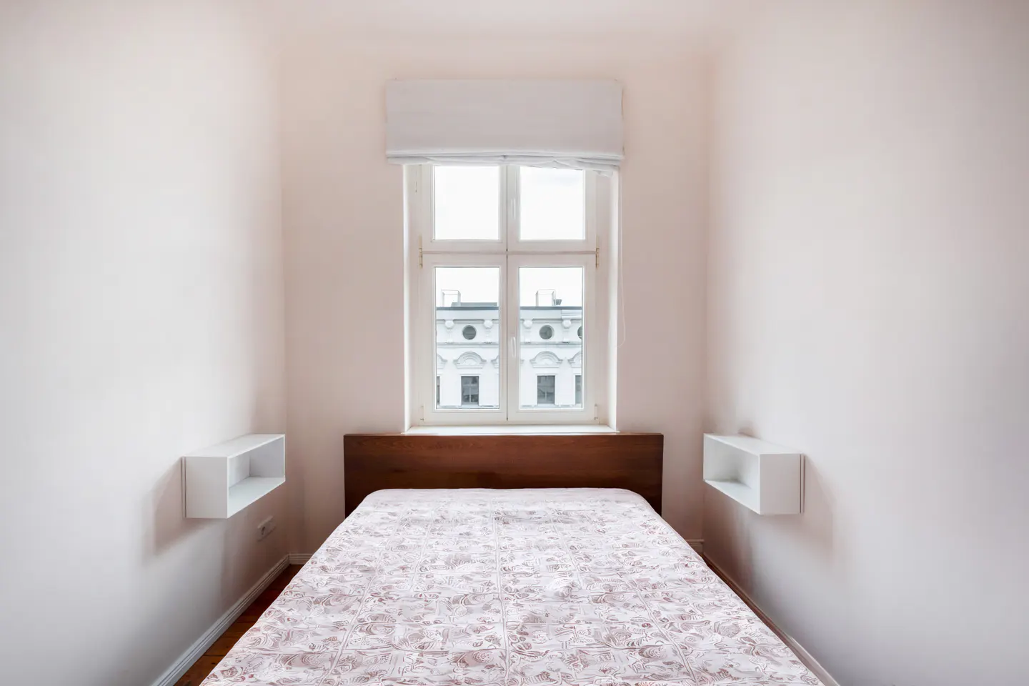 A bedroom with a bed, a window, and two white shelves on the walls.