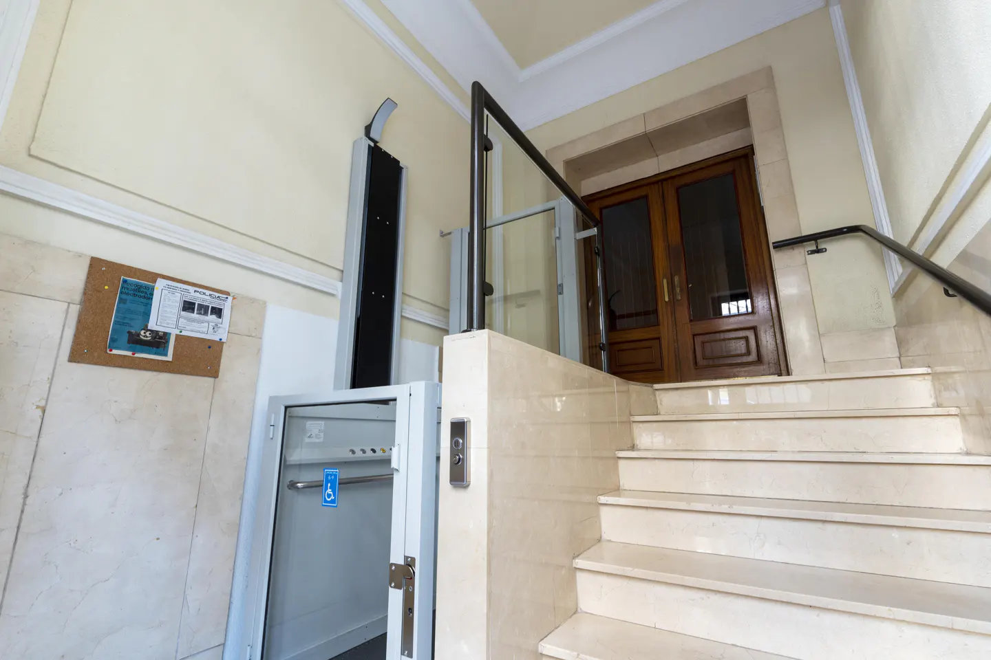 Interior view of a building entrance with stairs, a lift for disabled access, and a wooden door.