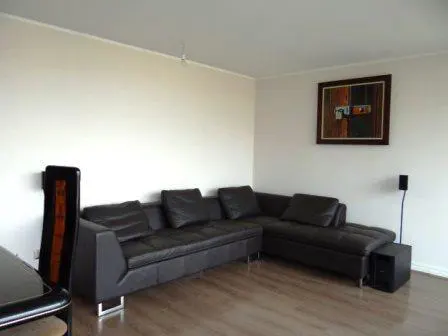 Living room with a black leather sectional sofa, wood floors, and white walls. A framed abstract painting hangs on the wall.