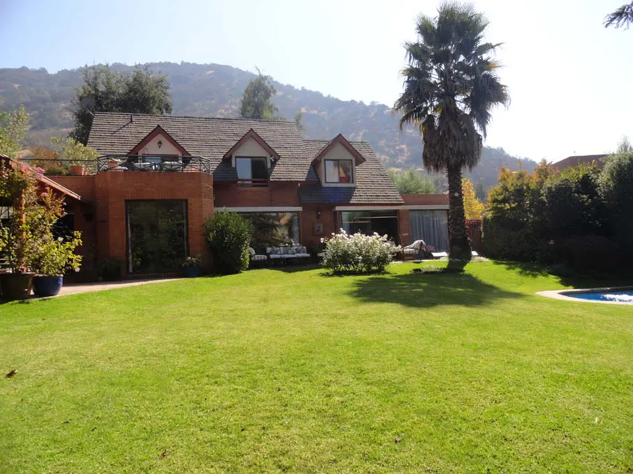 Brick house with a brown roof, large windows, and a green lawn. A palm tree stands to the right of the house.