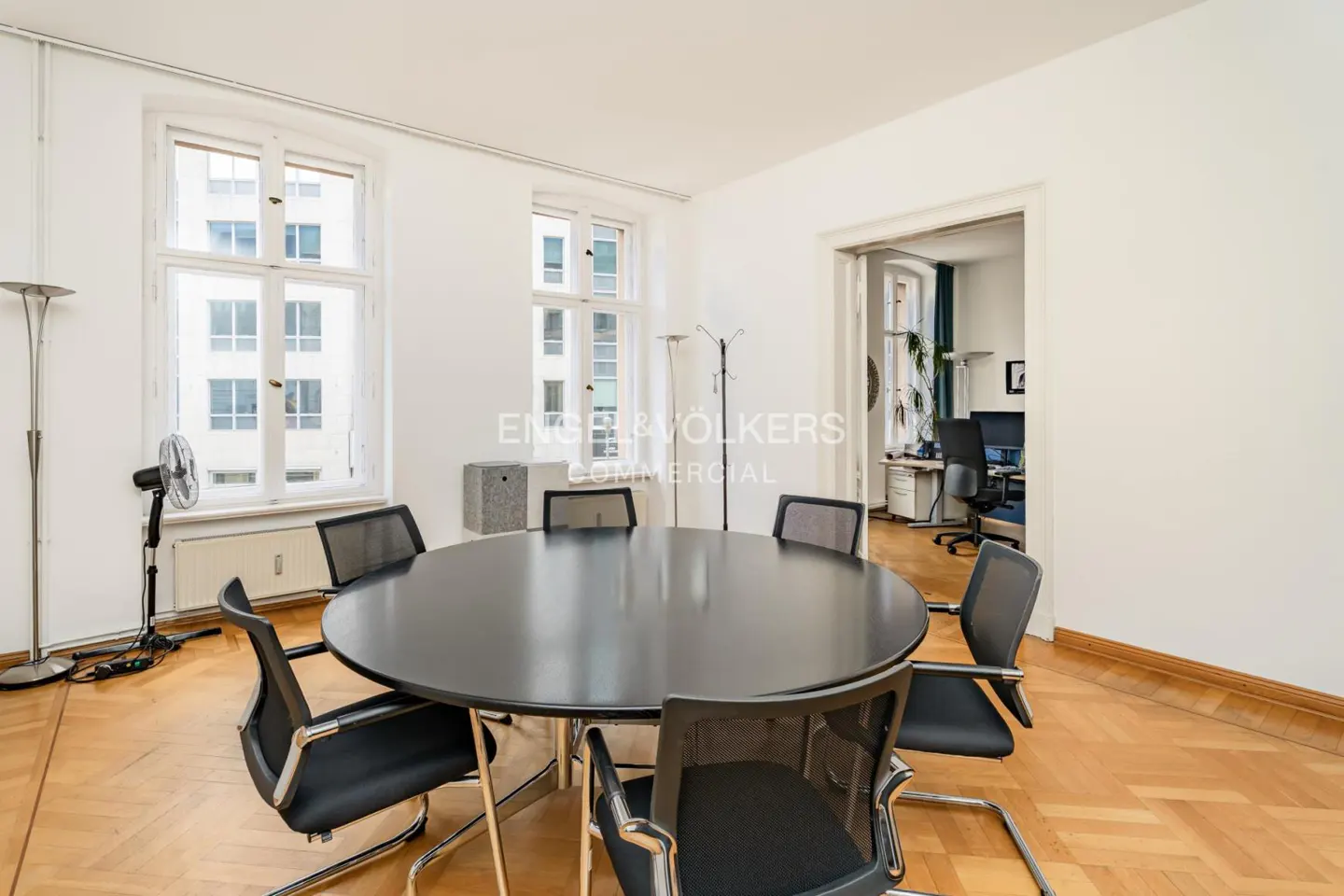 Bright office meeting room with a round black table, four black chairs, parquet flooring, and large windows.