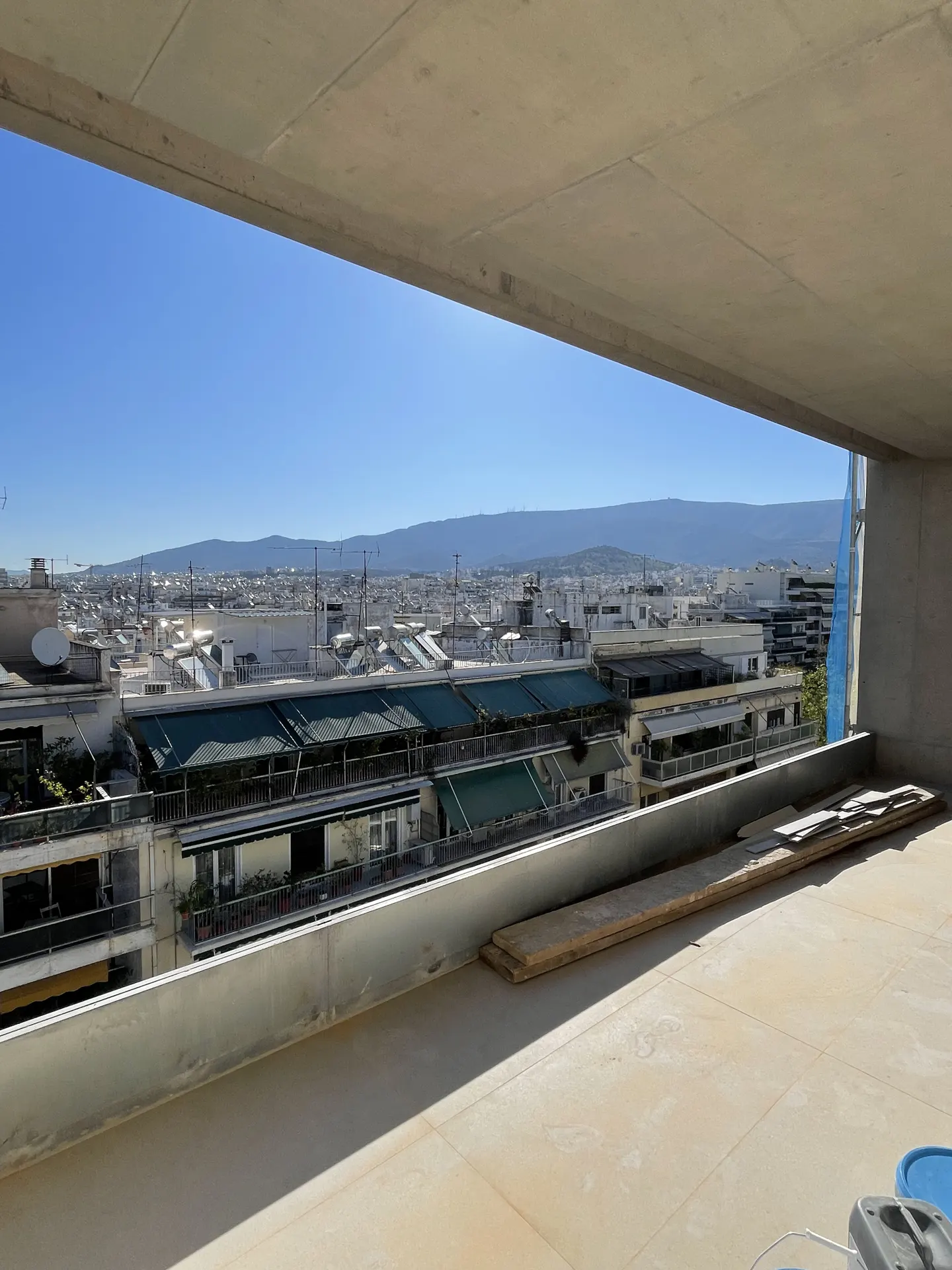 View from a balcony overlooking a city with buildings and mountains under a blue sky.