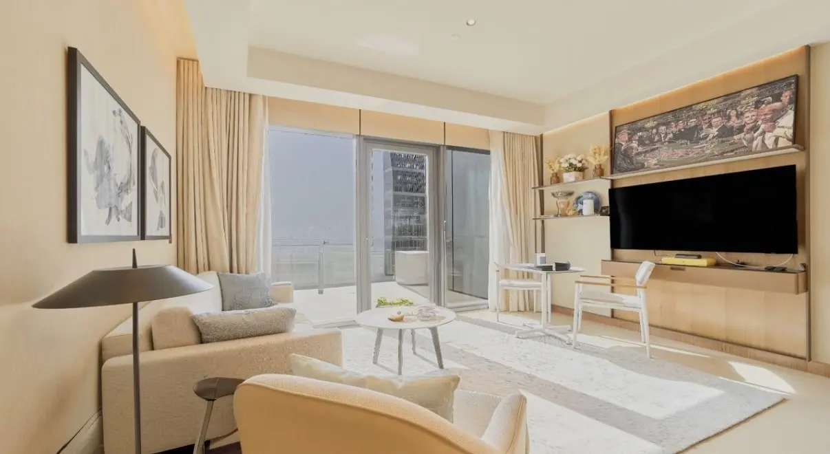 Modern living room with beige sofa, armchair, coffee table, wall-mounted TV, and floor-to-ceiling windows with balcony view.
