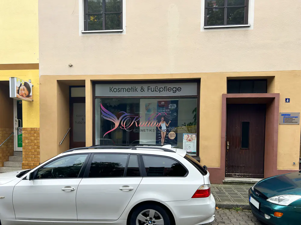 A beige storefront for a beauty salon named "Kalluri" with a white station wagon parked in front on a city street.