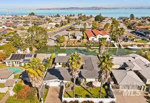 Aerial view of a waterfront neighborhood with houses, canals, and palm trees under a blue sky.