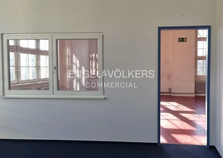 Empty room with a window and a blue-framed doorway. The floor is blue and red. The Engel & Völkers logo is on the wall.