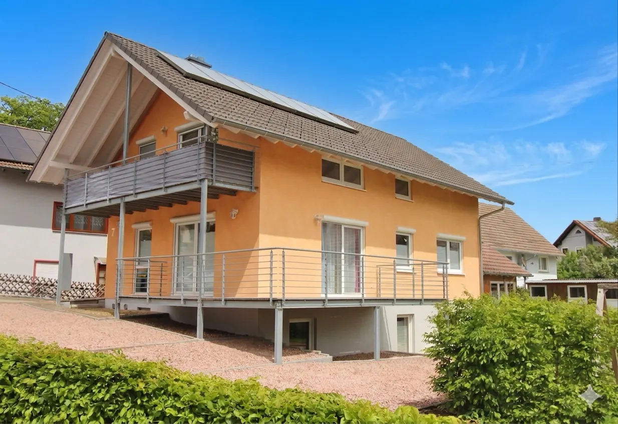 Two-story peach house with gray roof, solar panels, and metal balconies under a blue sky.