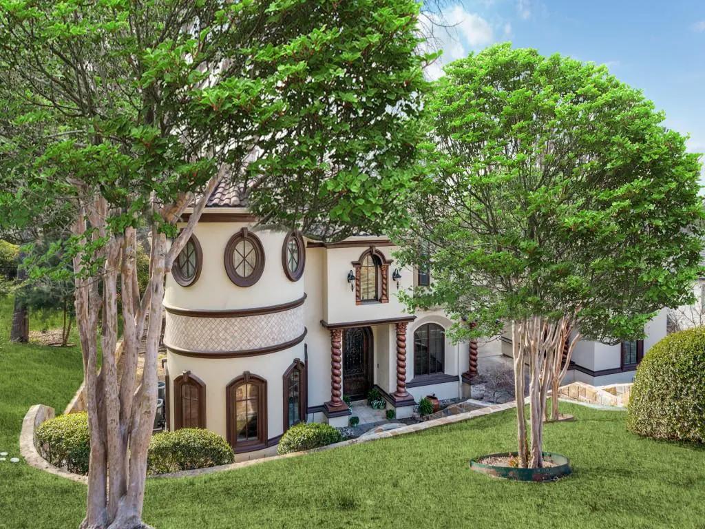 Exterior view of a cream-colored house with a turret, brown trim, and green lawn, framed by trees.