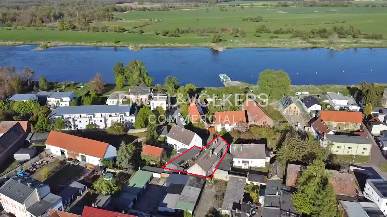 Aerial view of a property outlined in red, near a river and green fields, surrounded by other buildings and trees.