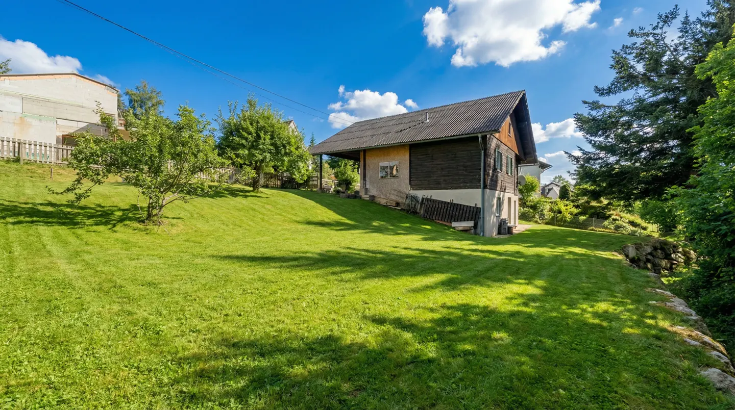 Exterior view of a two-story house with dark wood siding and a large green lawn on a sunny day.