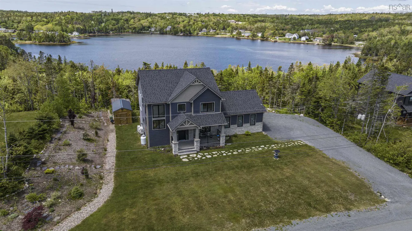 Two-story blue house with gray roof, green lawn, and lake view. A shed sits to the left of the house.