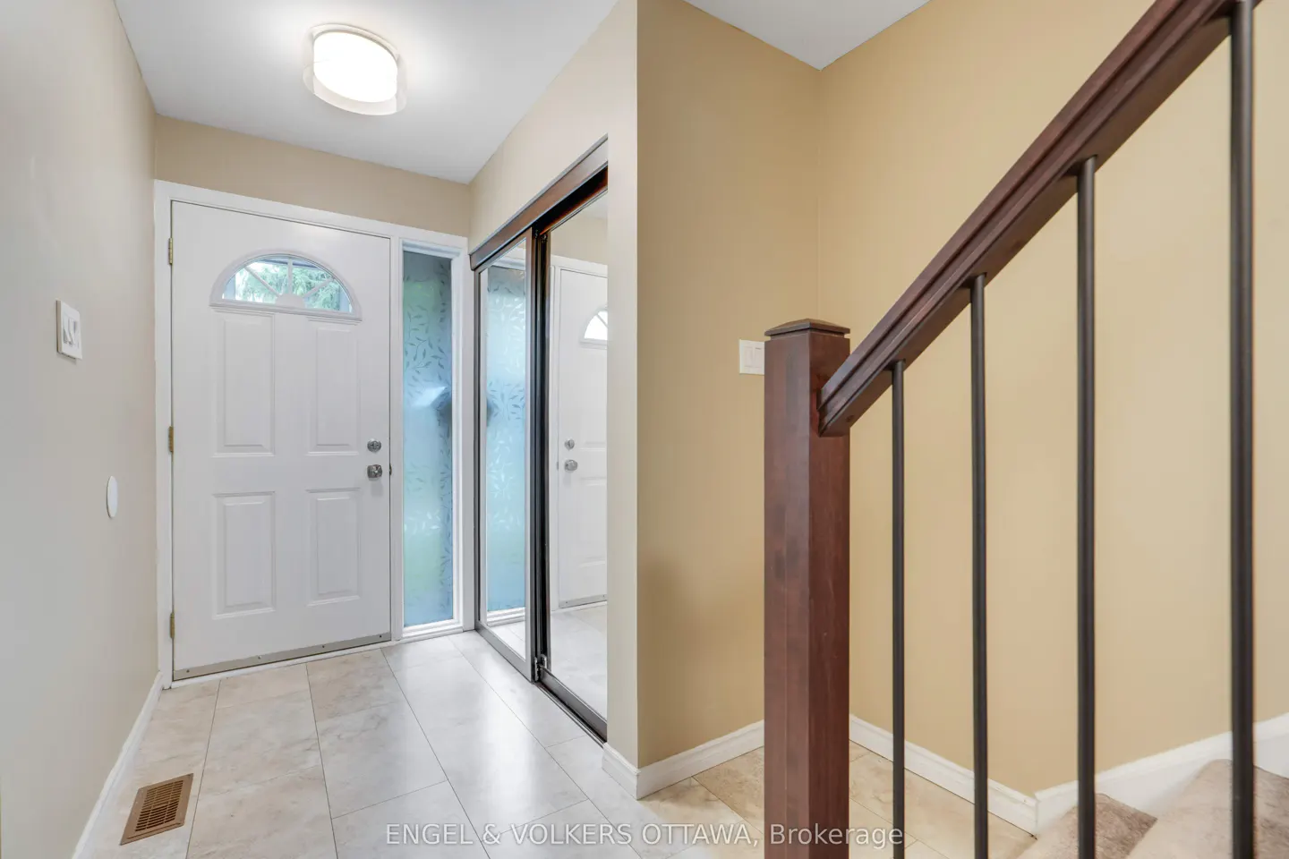 A home's foyer with a white front door, a sliding door, and a staircase with a dark wood railing.