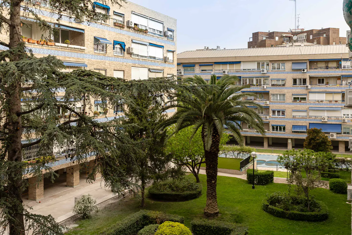 View of apartment buildings surrounding a green courtyard with trees and a pool.