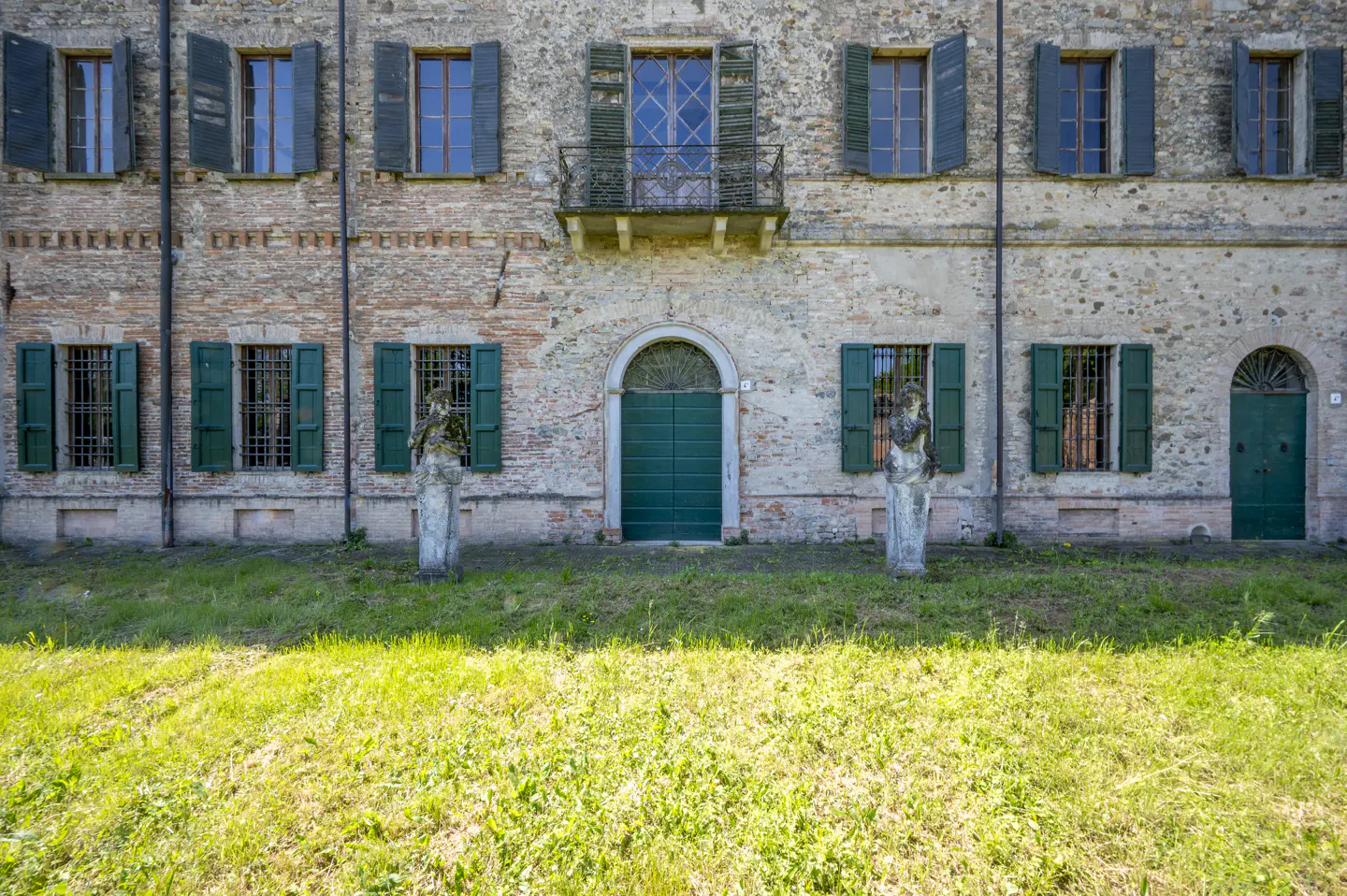 Exterior view of a two-story brick building with green shutters and doors, and a green lawn in front.